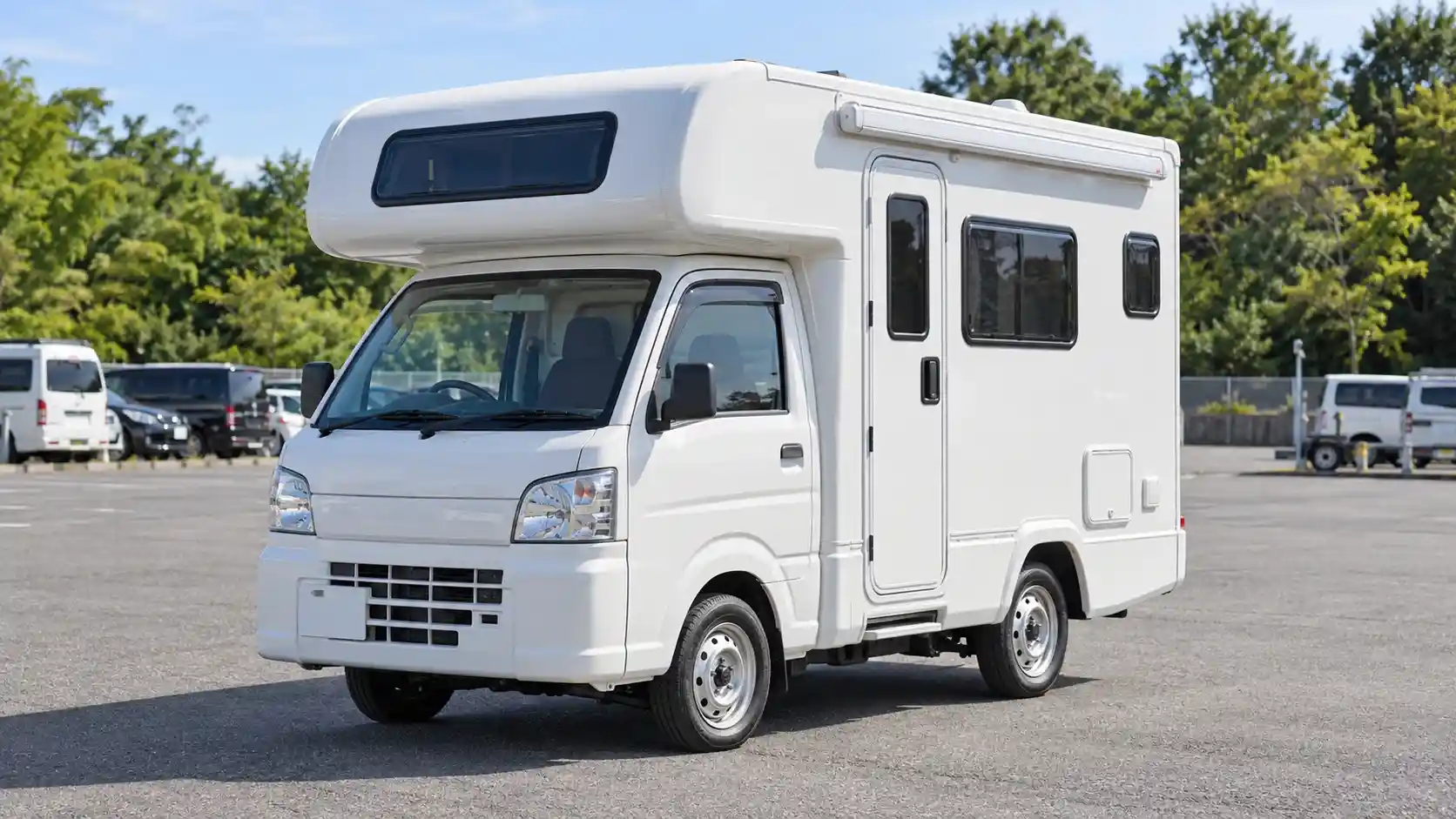 White compact camper parked in a vehicle yard with trees in the background.